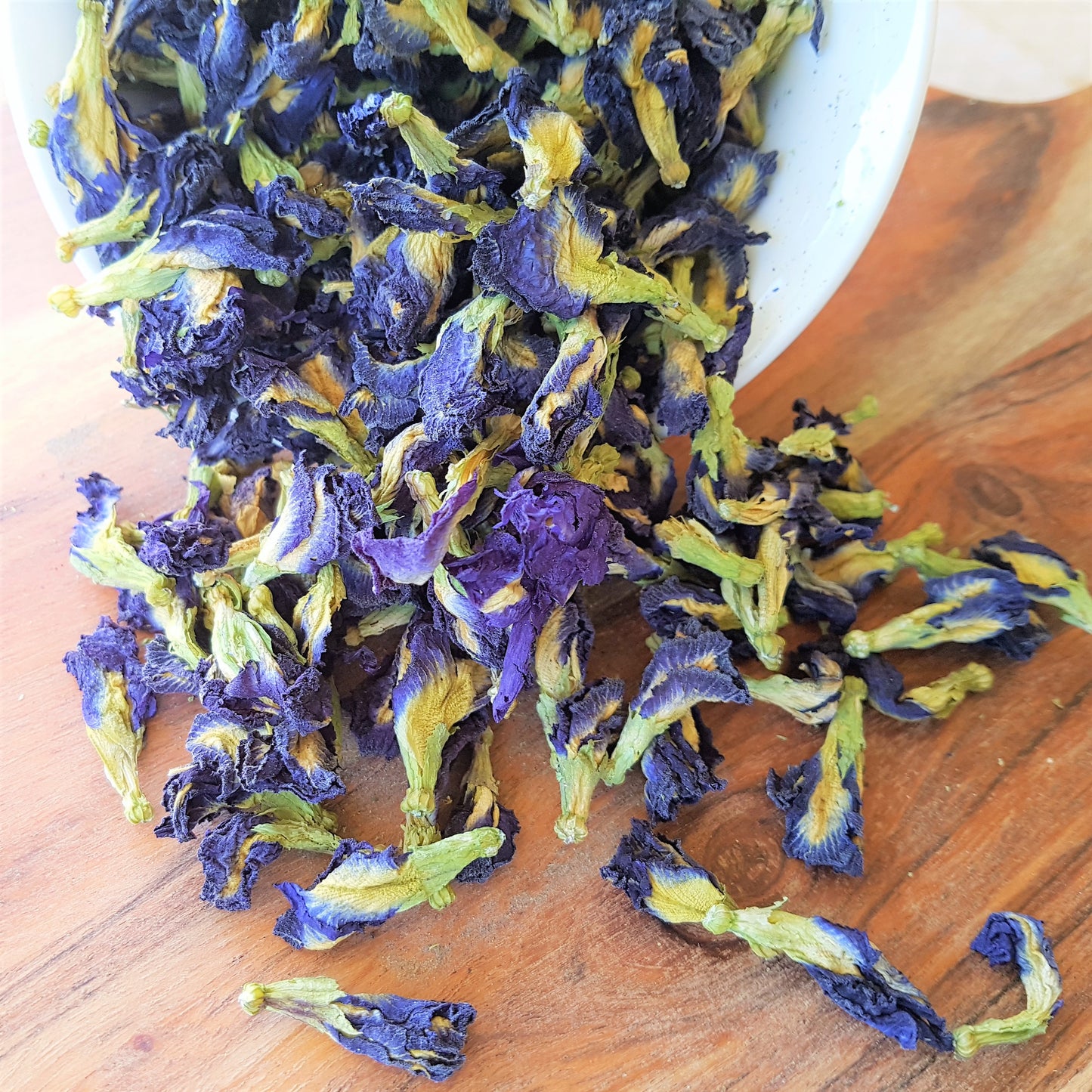 organic butterfly pea flowers spilling out of a bowl onto a wooden board