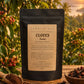 A black stand-up pouch of Sunrise Tea Cloves Powder with a beige label, photographed on a white fabric surface.