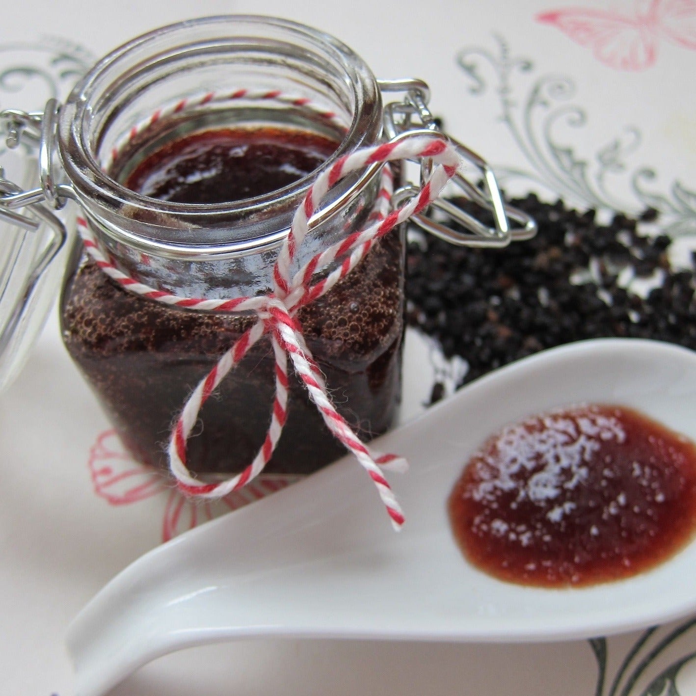 Elderberry jam in an open glass jar. A sampling has been taken out on a large flat white spoon.