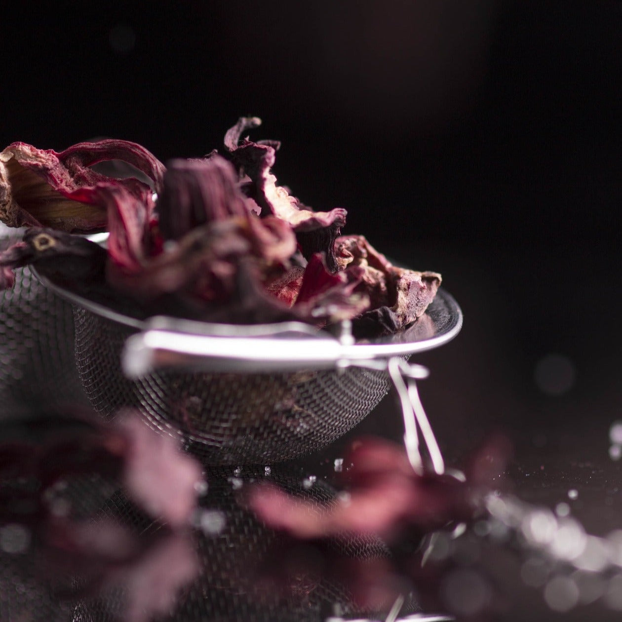 Stylistic close up shot of hibiscus flowers inside a sieve swishing atop water. Foreground is blurred.