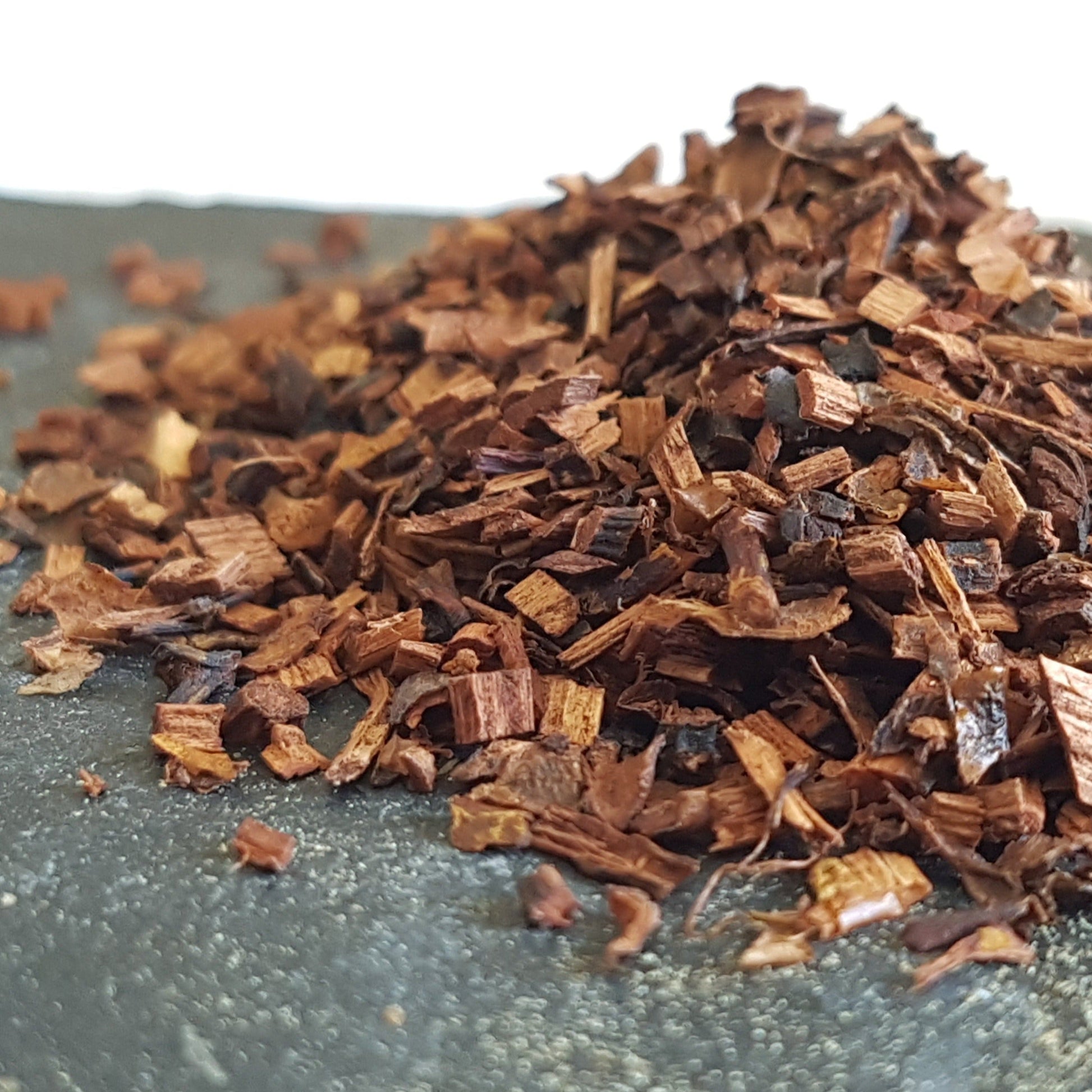 Dried reddish brown honeybush tea on grey slate is ready for tea making. Has antioxidants. Helps fight cancer, fat cells, menstrual symptoms, promotes skin and bone health and potentially helps with diabetes.