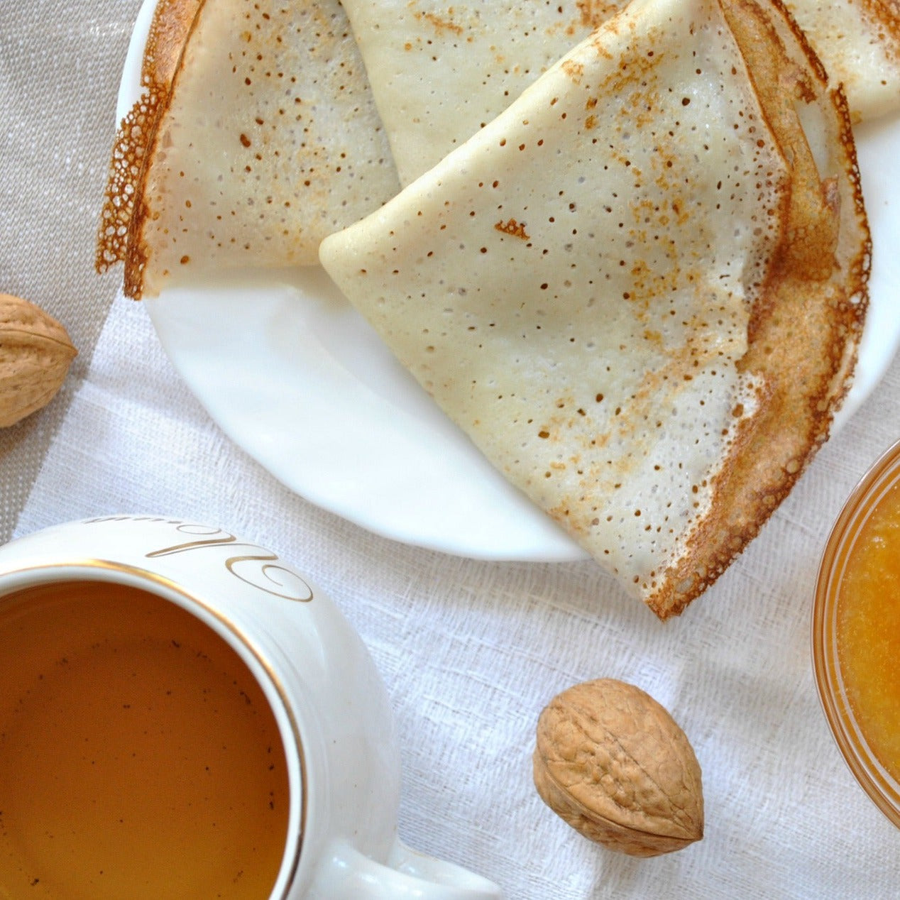 A pretty stylised top down view of a crepe breakfast. Honeybush tea in white mug is a golden honey colour.