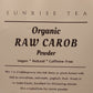 A close-up of a product label for Sunrise Tea Organic Raw Carob Powder, showing the text on a white background against a dark background.