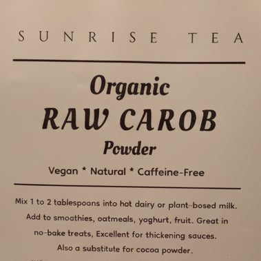 A close-up of a product label for Sunrise Tea Organic Raw Carob Powder, showing the text on a white background against a dark background.