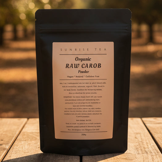 A black stand-up pouch of Sunrise Tea Organic Raw Carob Powder with a beige label, photographed on a white fabric surface.