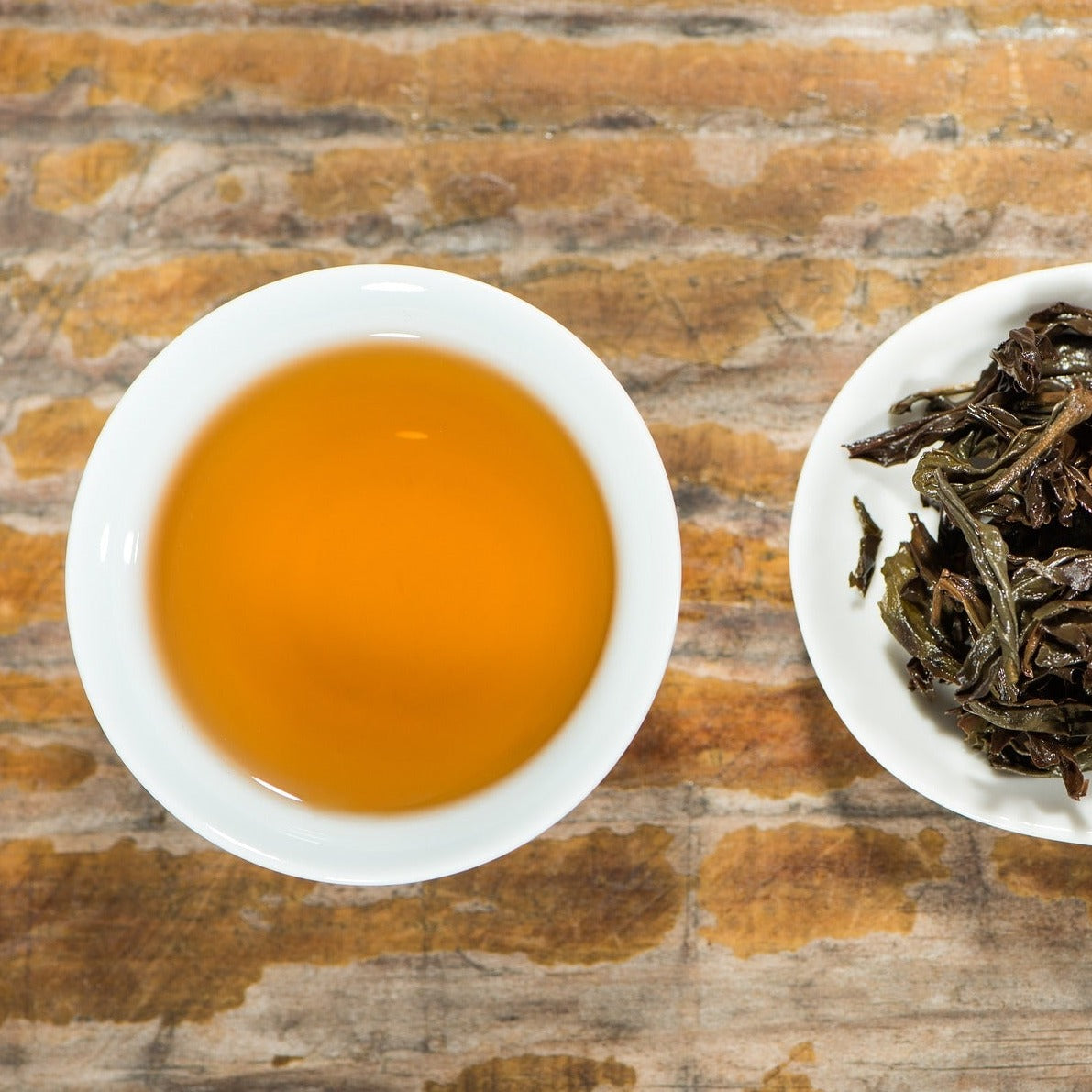 Earl grey tea served up in a white tea cup without handles. Next to the tea cup is an elongated plate with the strained tea leaves glistening on the plate. Earl grey tea contains antioxidants and good for the heart and digestion.