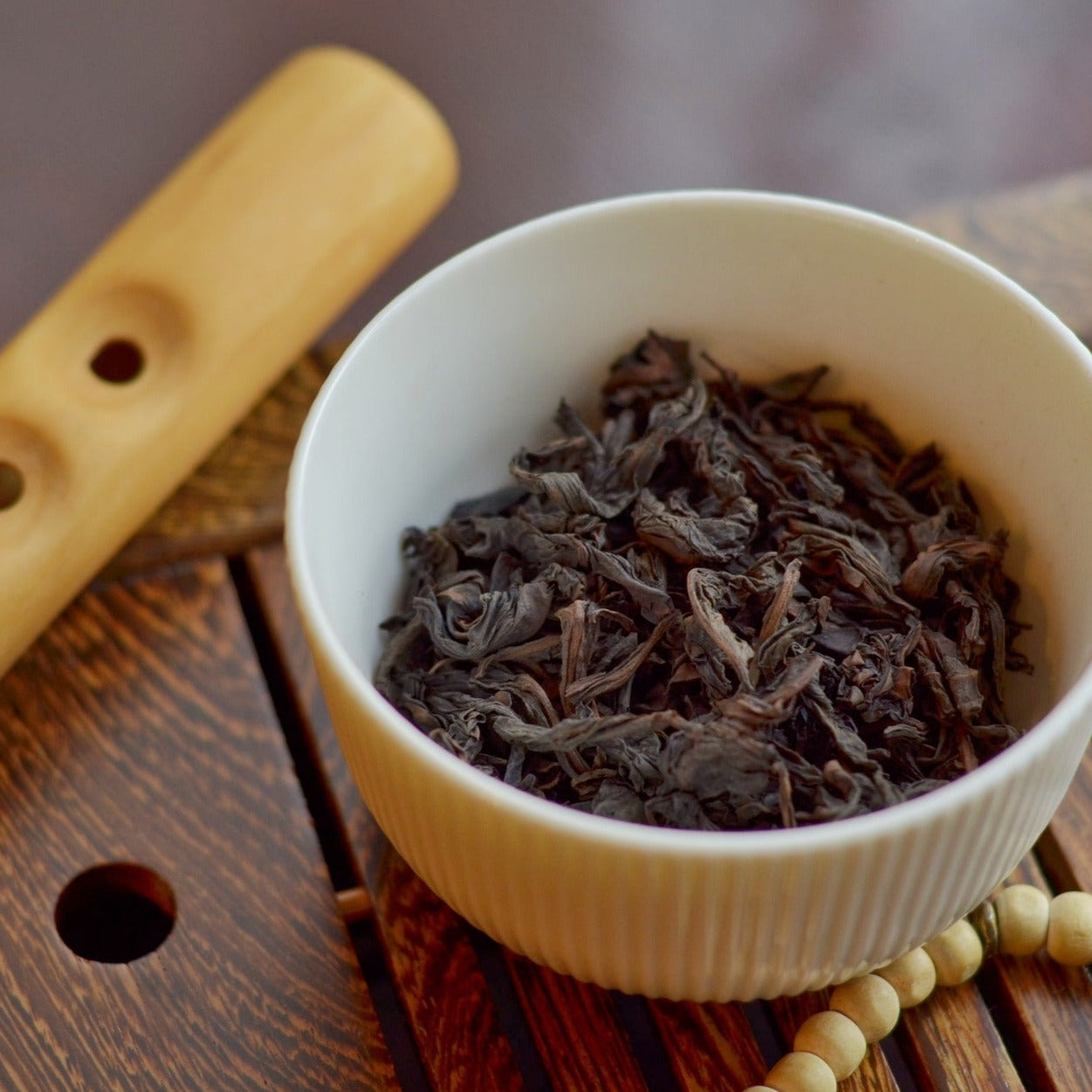 Close up of darjeeling tea in a petite ribbed bowl. Flute in background and also wooden stringed beads. All on a wooden slotted tray.