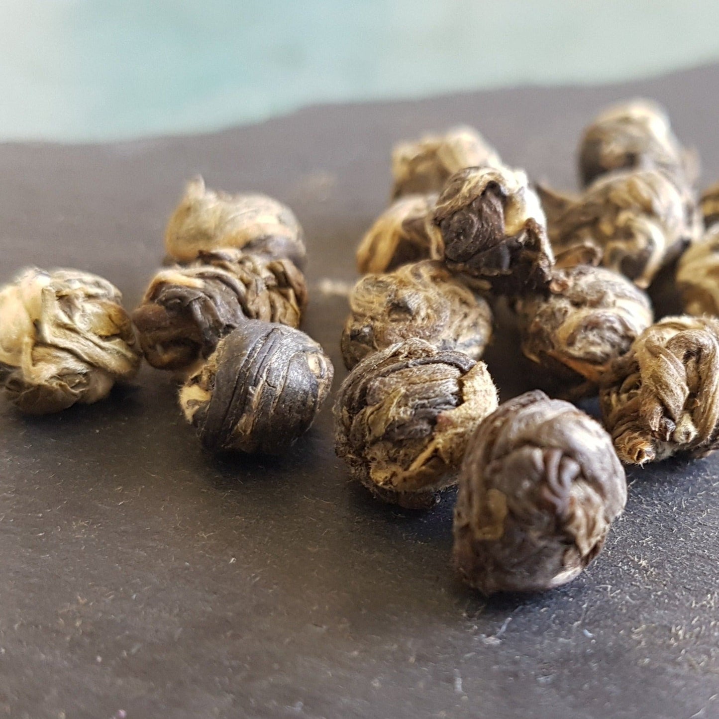 Close up shot of jasmine pearls green tea loose leaf tea. Shows how each pearl is tightly rolled up into a spherical form, presumably to trap the jasmine fragrance and nourishment. Colours are a light to dark brown.