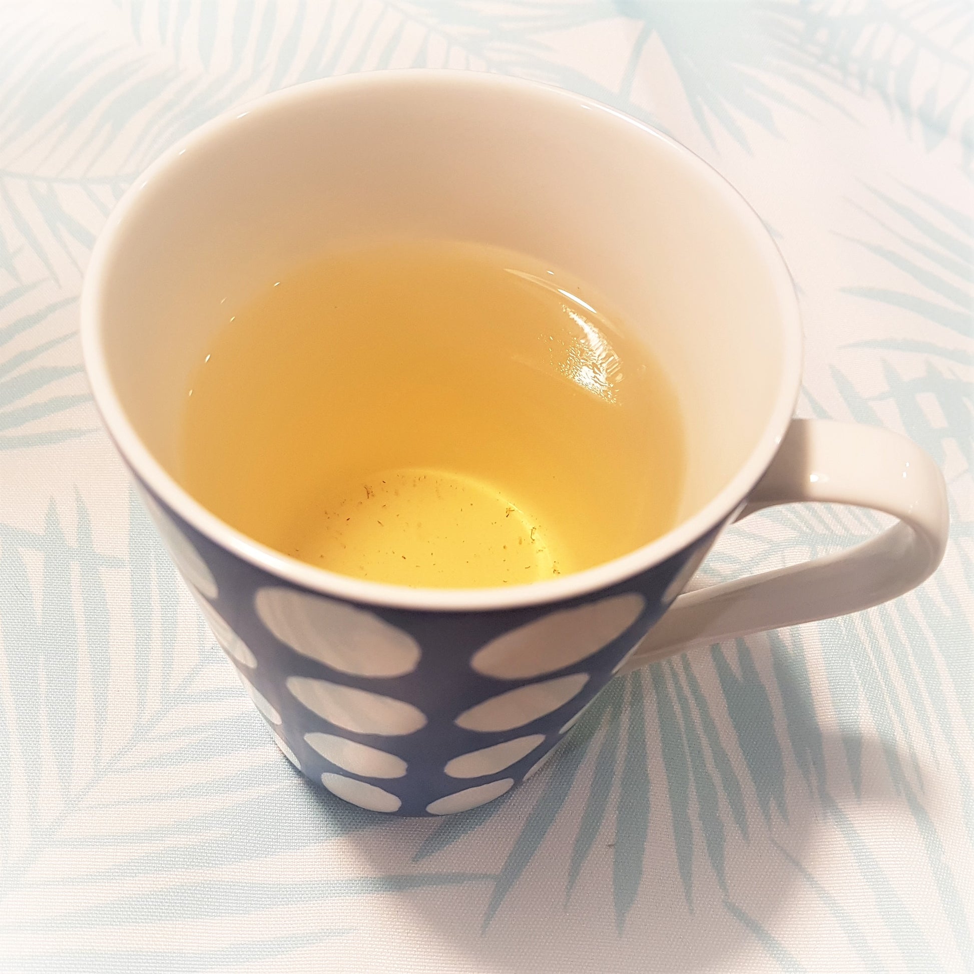 A photo of linden flower tea in a blue and white spotted mug. Tea is a pale yellow colour.