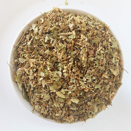 Dried Lindon flower tea in a bowl against a white background. Top down view provided. Looks like a mixture of linden flowers and leaves and bits of back of the linden tree. Colours are light green and brown.  Medicinal herbal tea mix which is said to assist against stress, anxiety, inflammation, pain, and high blood pressure. Diuretic effect also.