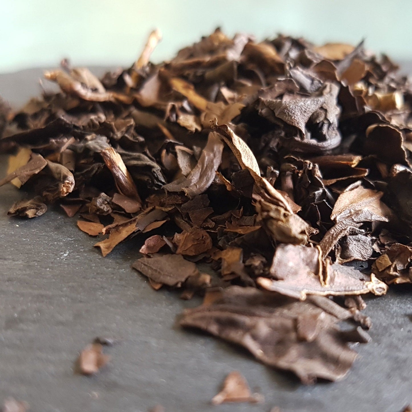 A pile of brown oolong loose leaf tea on a grey slate tile. Oolong is said to aid weight loss, lower blood pressure, improve sleep, be anti-hyperglycemic, improve gut microbiome, fight cancer, decrease vascular inflammation and protect the brain.