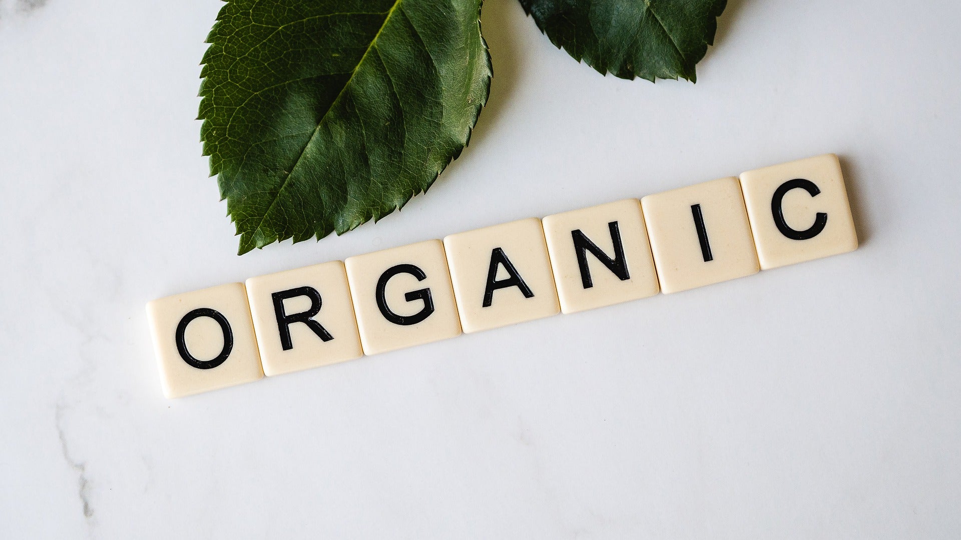 Our chamomile tea is 100% natural and organic. The word organic has been spelt out using Scrabble lettering. Green leaves decorate the photo.organic