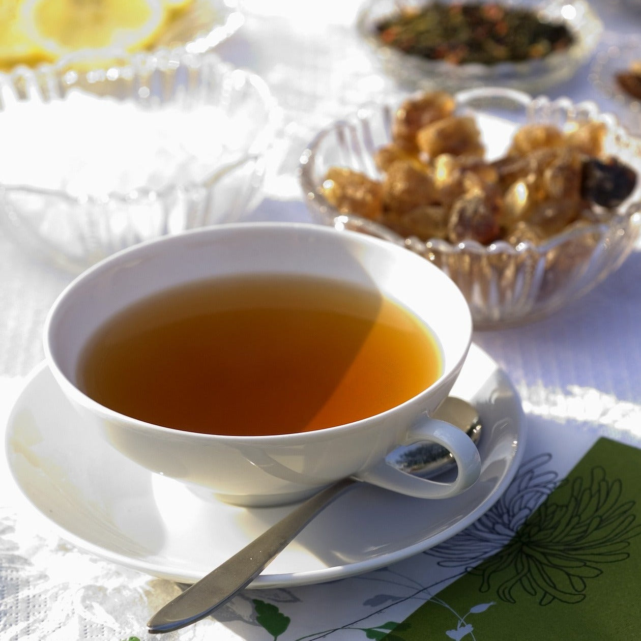 Darjeeling tea brew served in wide mouthed tea cup and saucer. Snacks in small crystal bowls in the background.